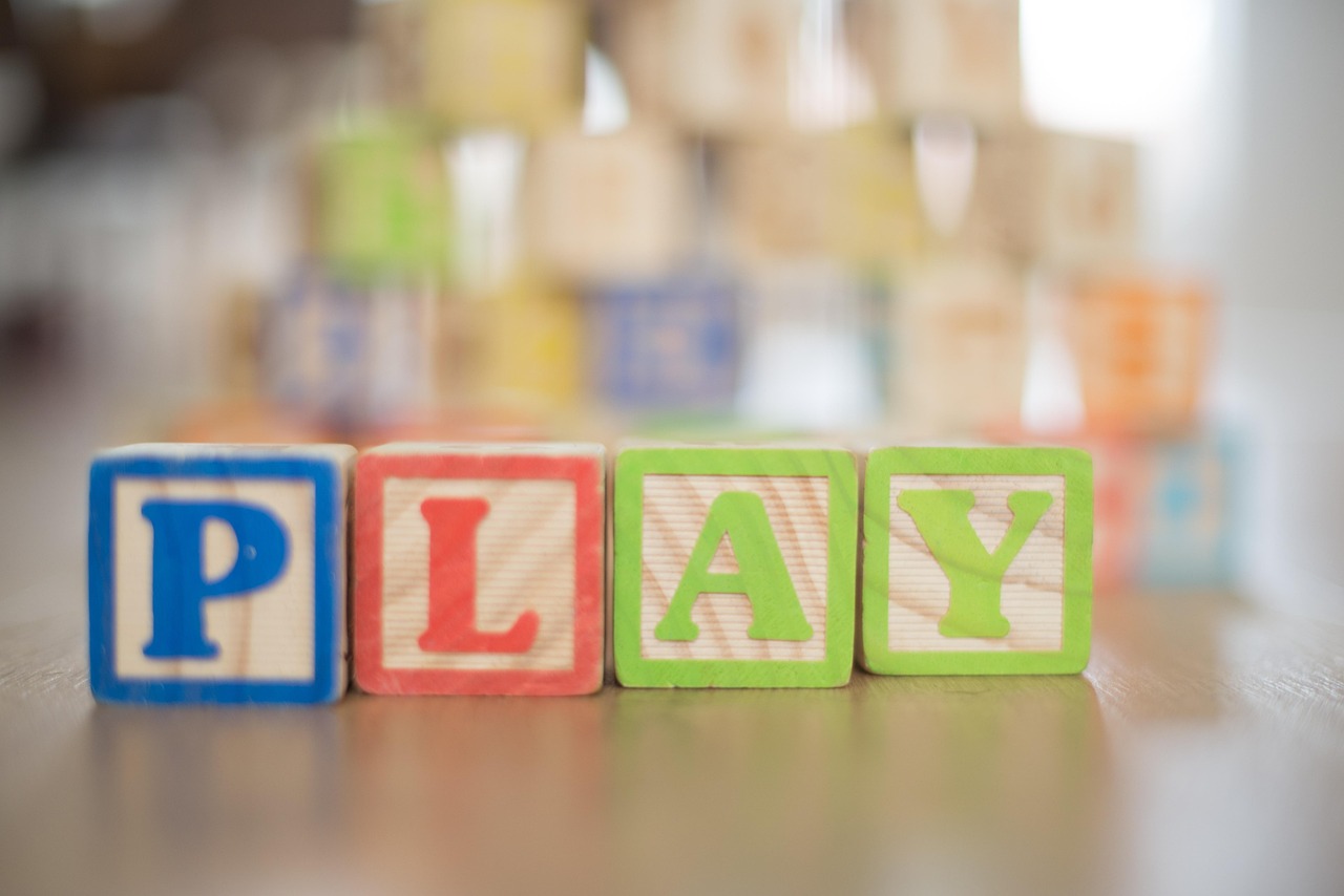 Wooden cubes, with coloured letters carved onto them, spell out the word PLAY in blue, red and green.