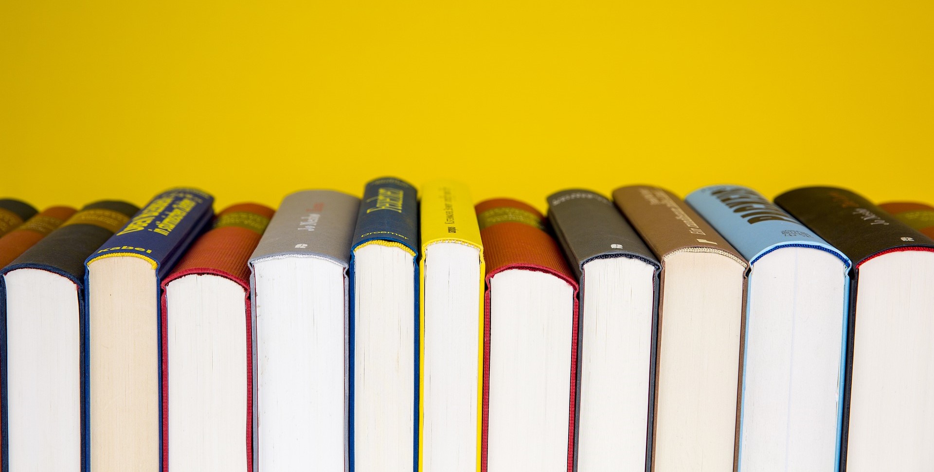Books, with the underside facing the camera, and spines in different colours just visible. Yellow background.