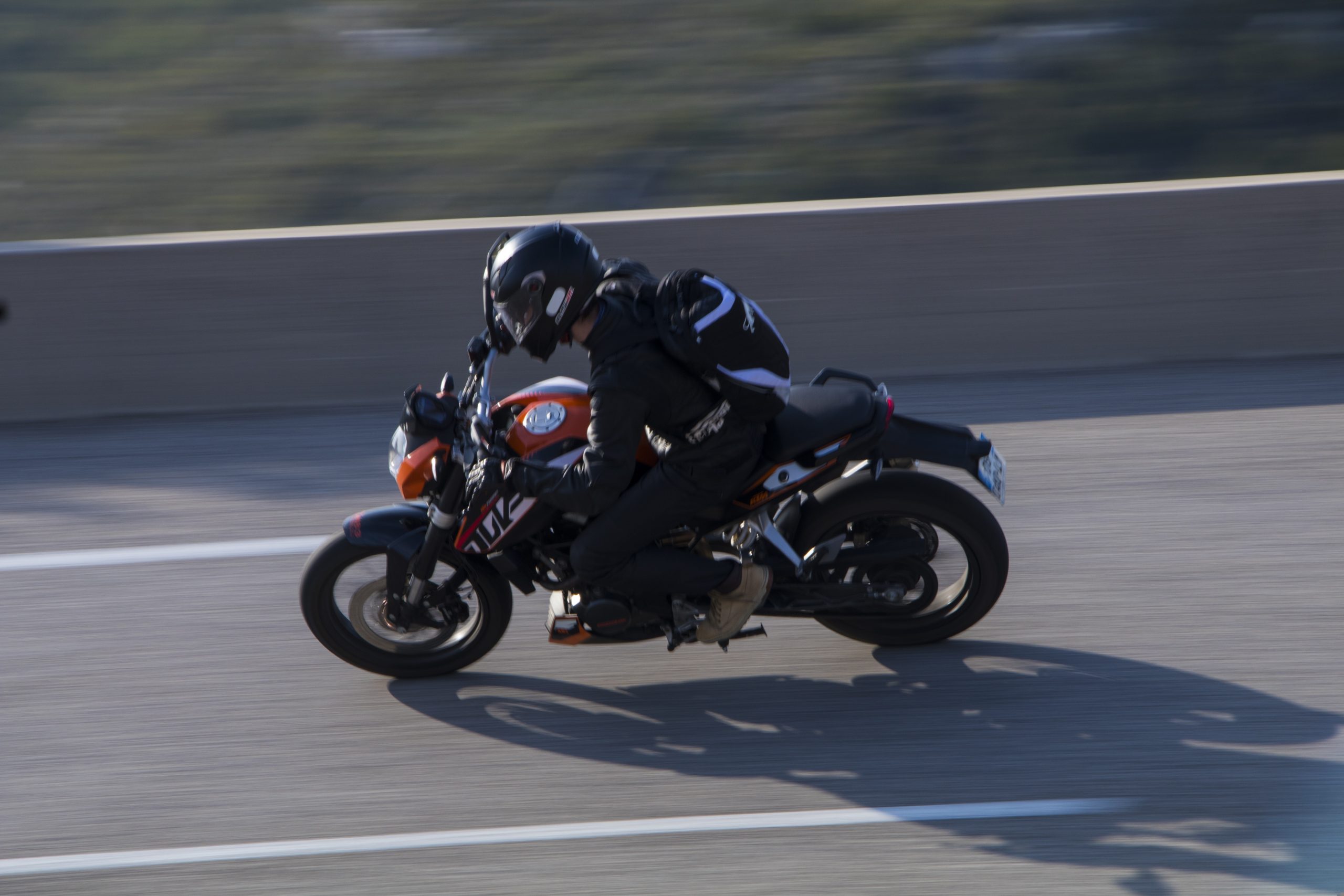A person wearing dark clothes and a black helmet rides a red motorbike. They are lent forward and the background is blurred giving an impression of speed.