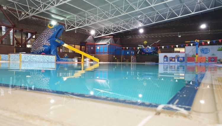A photo of Dalton Leisure Centre pool. A giant blue frog has a yellow slide from its mouth into the water