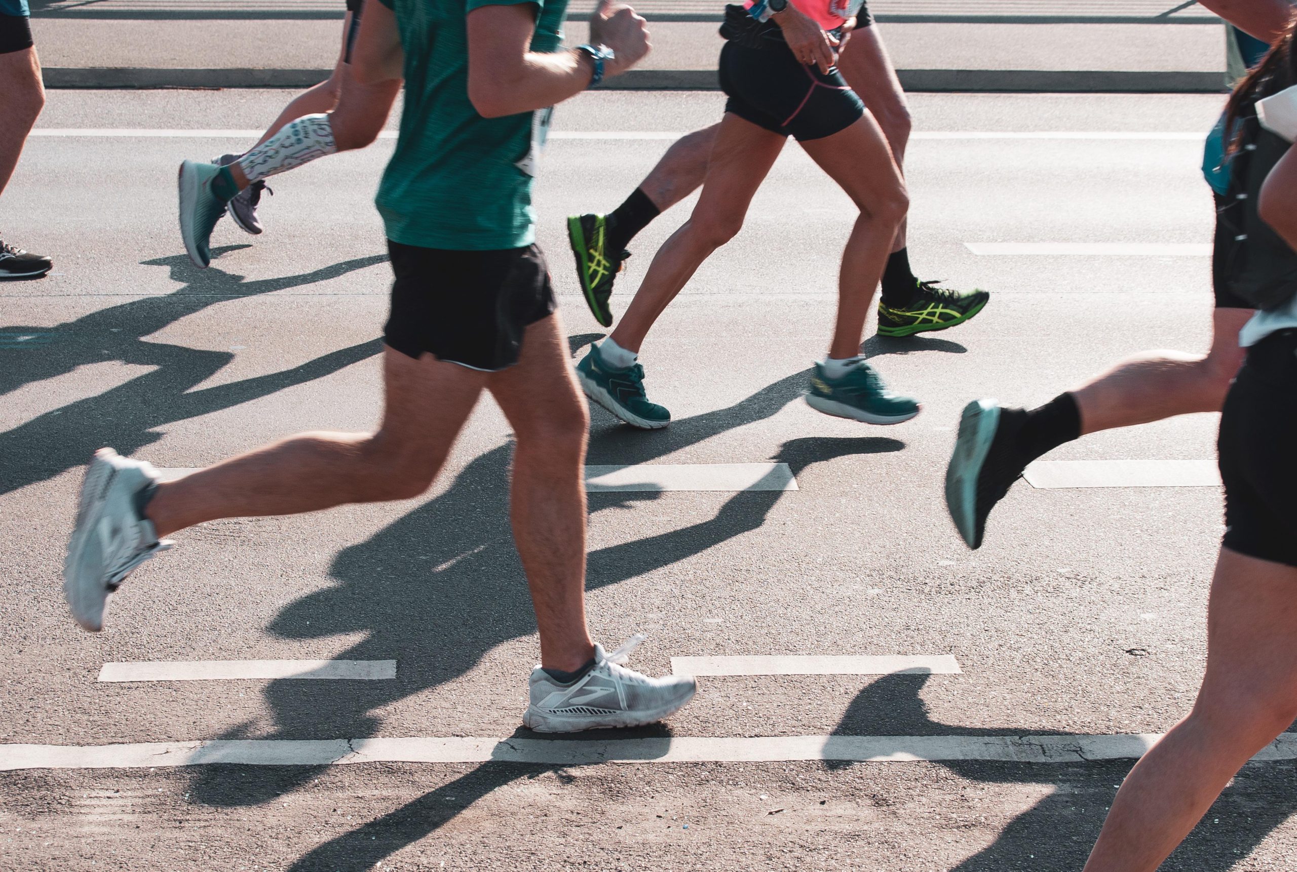 A close up image of runners in shorts running on a road surface. Only their lower halfs/legs are visible.